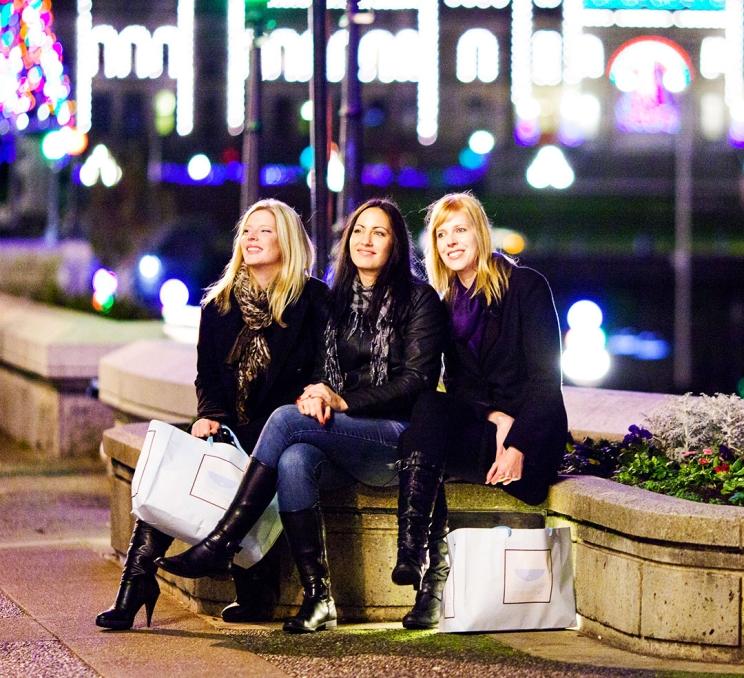 A group of three women take a seat along the Inner Harbour while shopping in downtown Victoria, BC