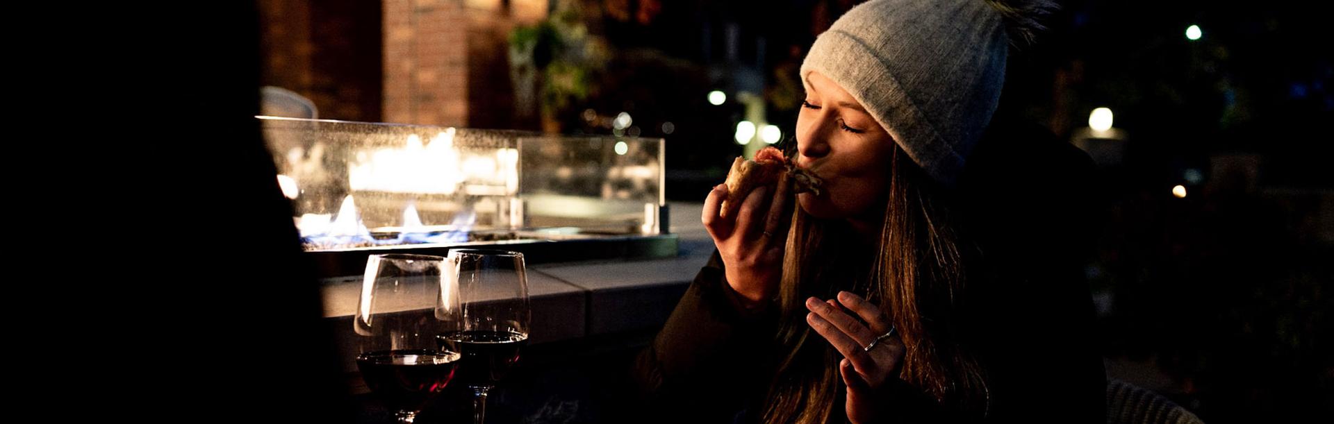 A woman bites into a slice of pizza on the patio during with winter at FARO Handcrafted Pizza and Tasting Room in Victoria, BC