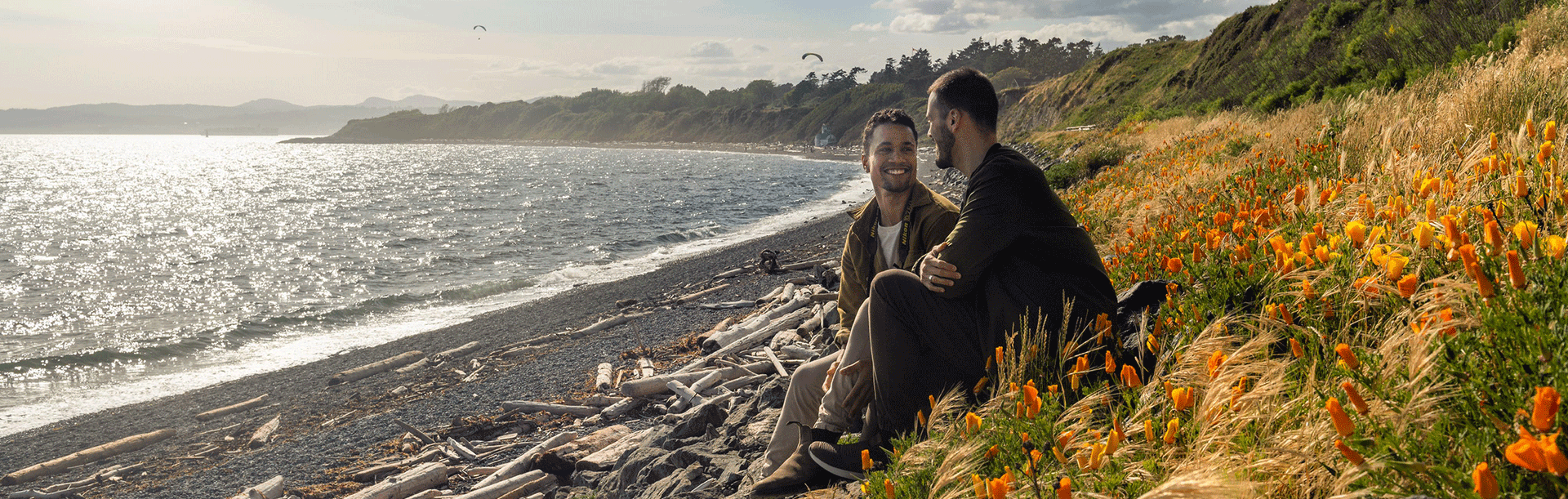 A male couple sits amidst the wild flowers on the beach at Clover Point in Victoria, BC