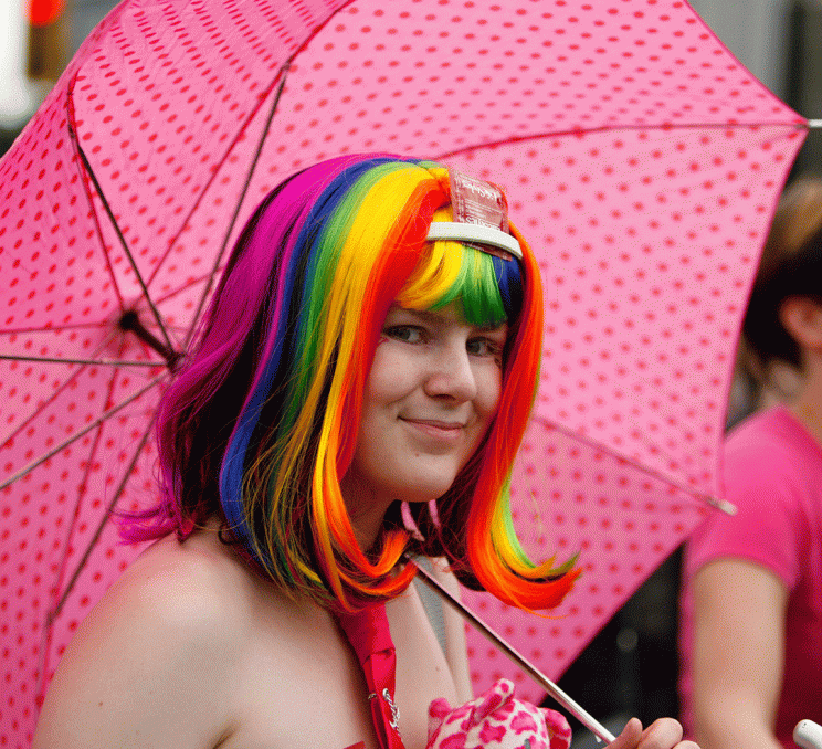 A person in a rainbow wig holding a pink umbrella celebrates at Victoria Pride Week in Victoria, BC