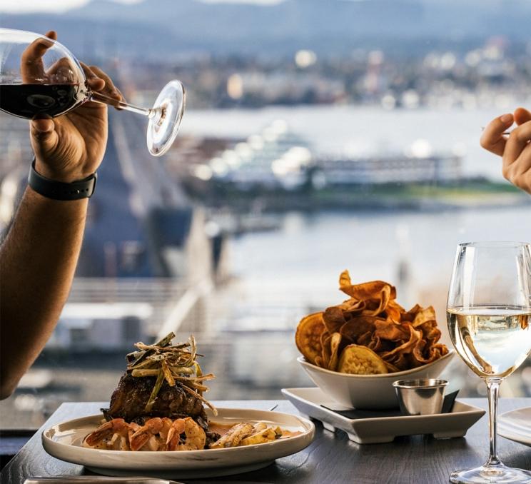 A couple dines on a steak and prawn dinner at Vista 18 a rooftop restaurant in Victoria, BC with views of the Inner Harbour