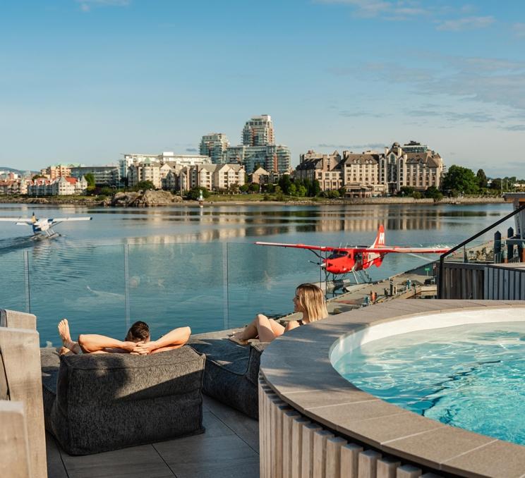 A couple sun bathes on the deck at HAVN Saunas watching the seaplanes at they take off from the Inner Harbour in Victoria, BC
