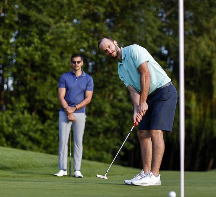 A man in a light blue shirt sinks a put on a golf course in Victoria, BC