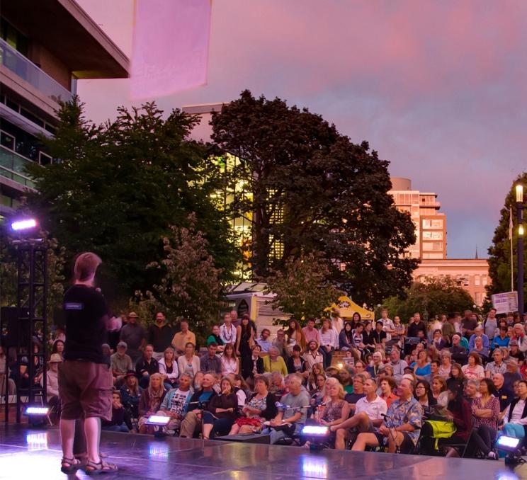 A performer on stage in front of a crowd of people in downtown Victoria, BC during the Fringe Festival