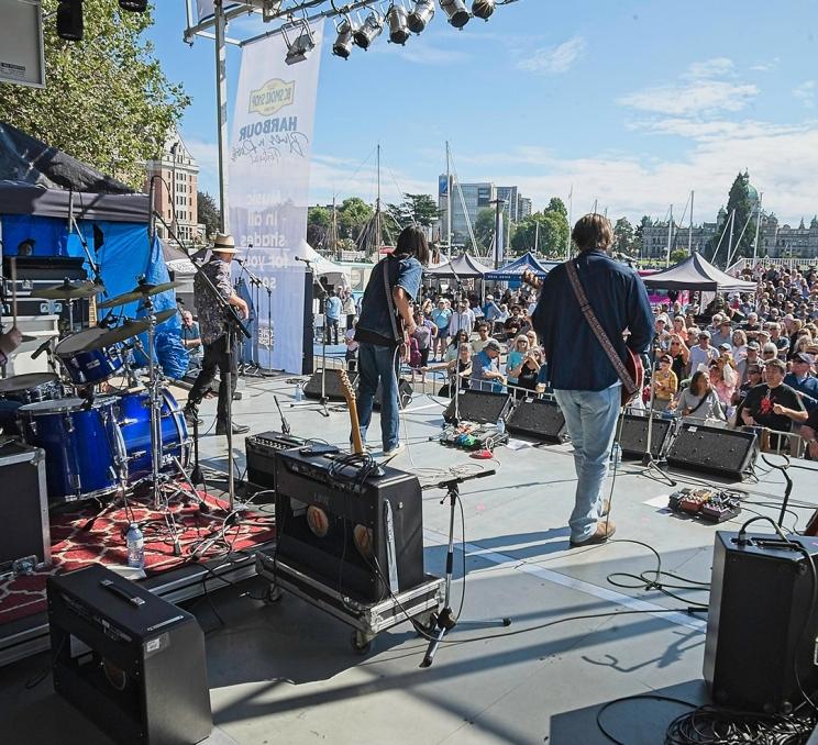 Three performers play their instruments on stage to a crowd at the Harbour Blues N' Roots Festival in Victoria, BC