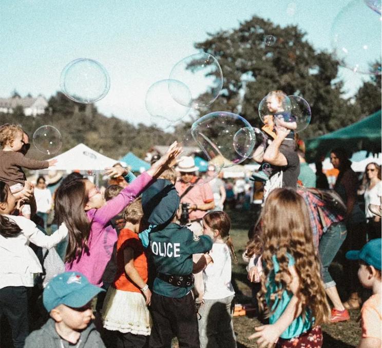 A group of families celebrate while bubbles fill the air at Fall Fairfield in Victoria, BC