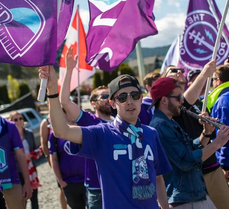 Pacific FC supporters dressed in purple wave club flags before a game in Victoria, BC