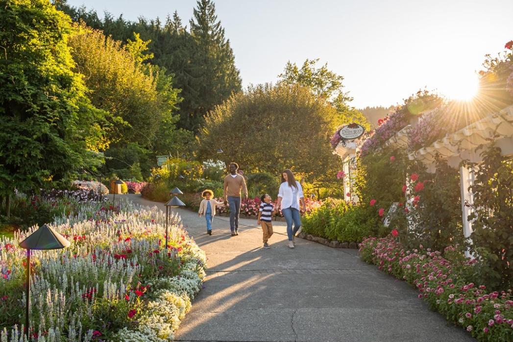 A mother and father walk hand-in-hand with their two young children down a path at The Butchart Gardens, a National Historic Site of Canada, in Victoria, BC