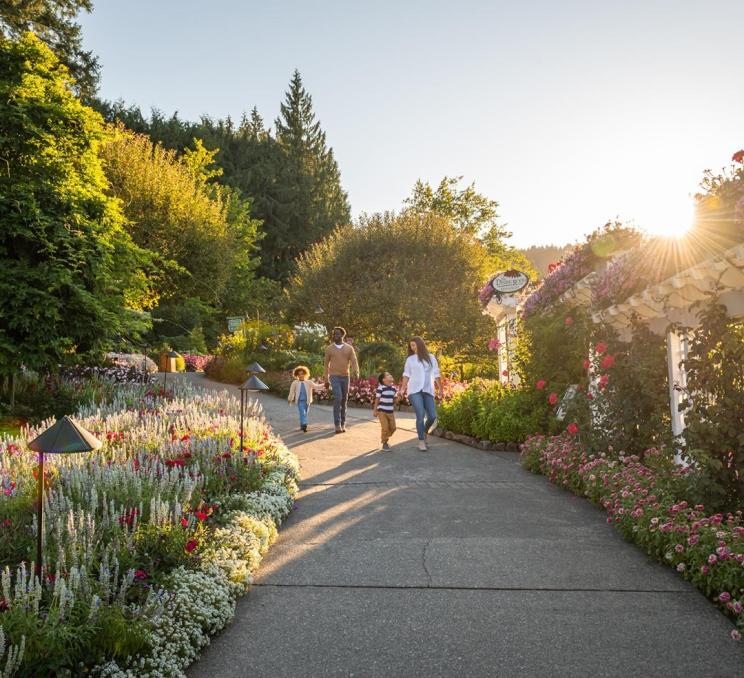 A mother and father walk hand-in-hand with their two young children down a path at The Butchart Gardens, a National Historic Site of Canada, in Victoria, BC