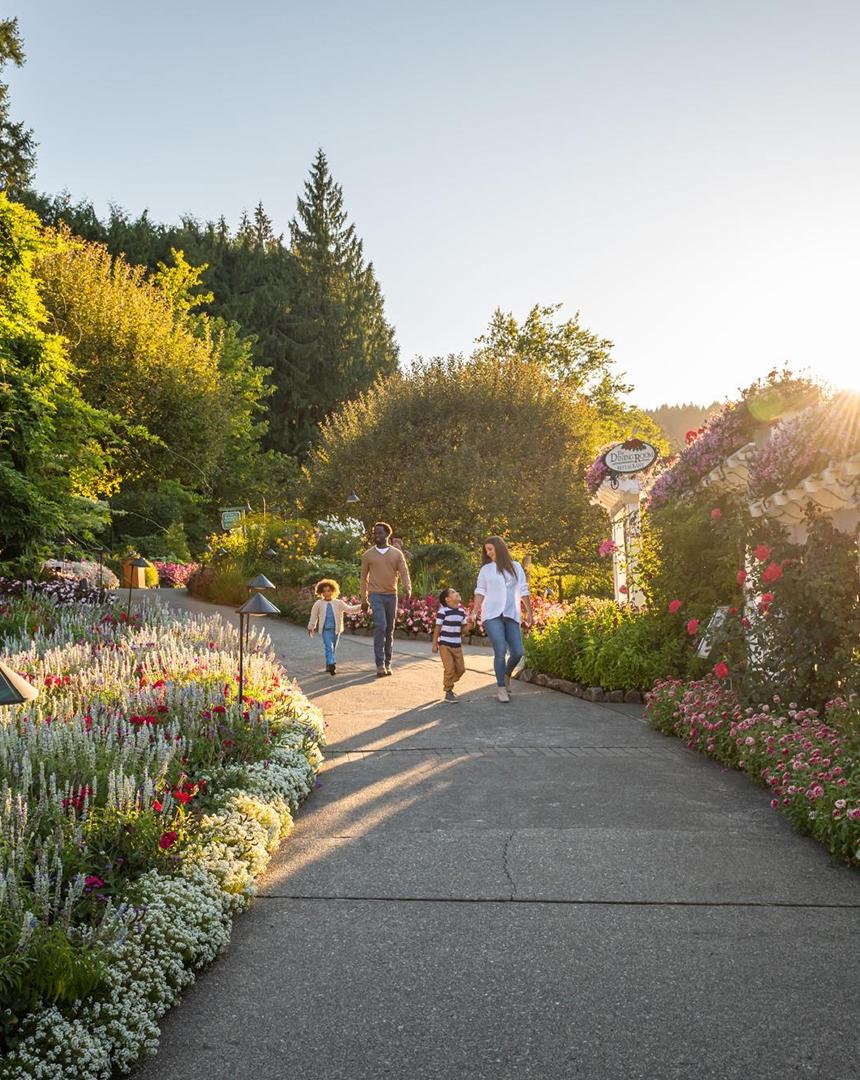 A mother and father walk hand-in-hand with their two young children down a path at The Butchart Gardens, a National Historic Site of Canada, in Victoria, BC