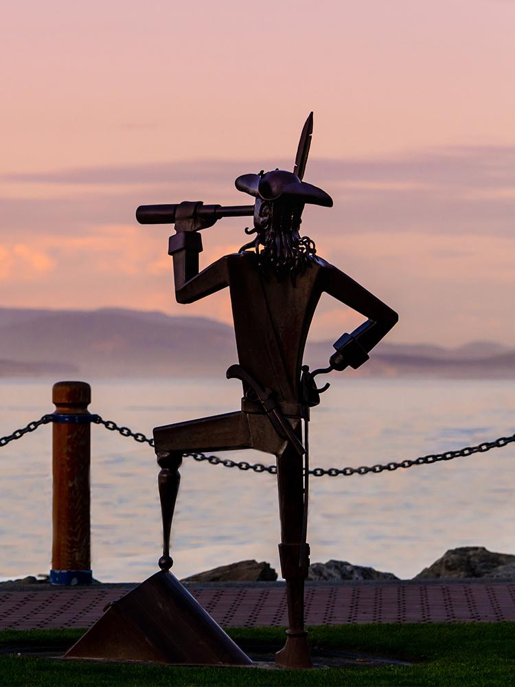 A pirate sculpture in Greater Victoria, BC at sunset overlooks the water of the Salish Sea