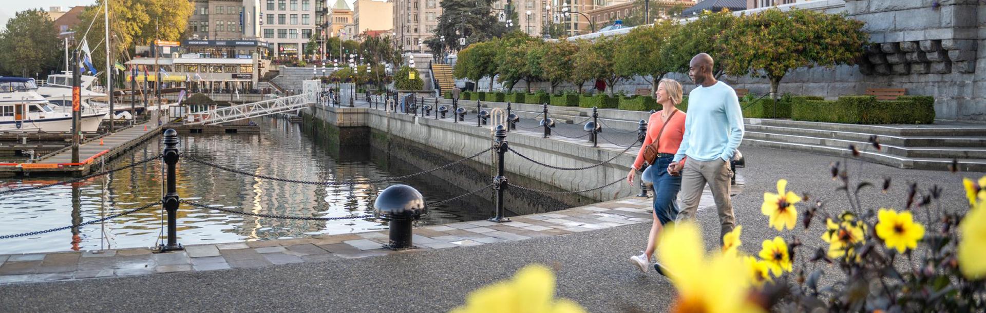 A couple walks hand-in-hand along the lower causeway of the Inner Harbour in Victoria, BC