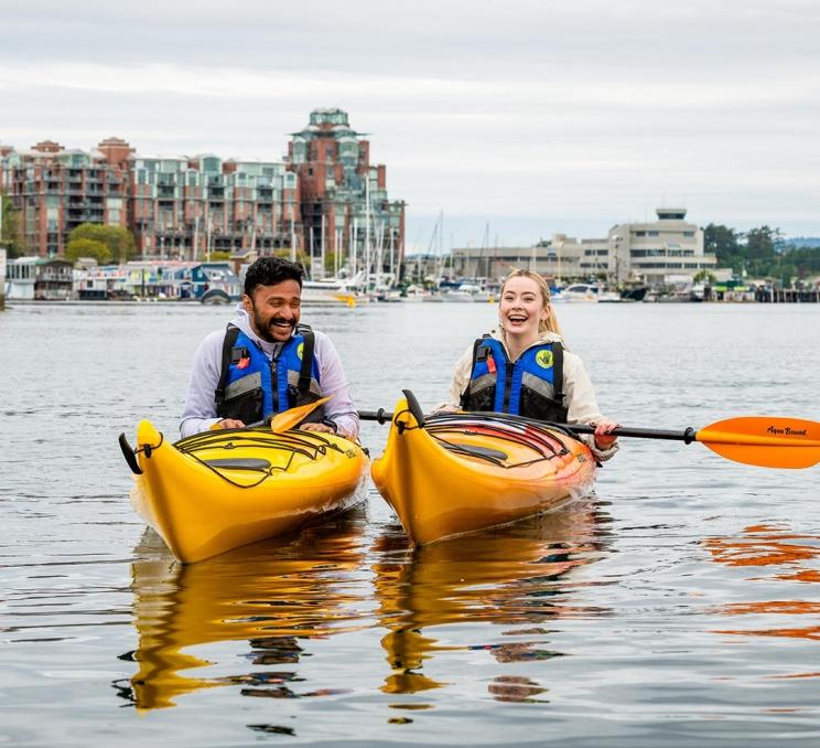 A couple kayaks in yellow kayaks across the Inner Harbour in Victoria, BC