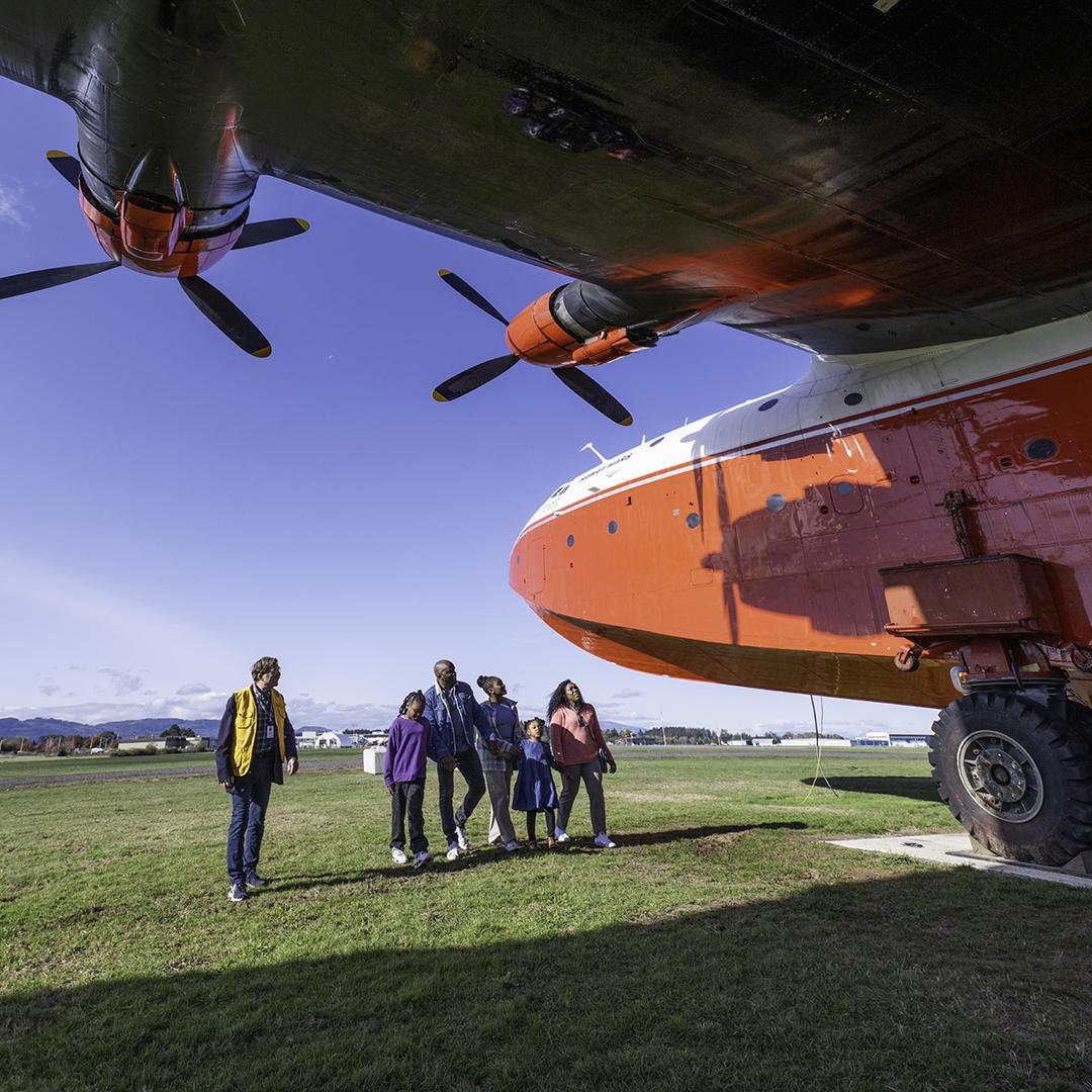 A family walks beneath the red and white Hawaii Mars waterbomber in Victoria, BC