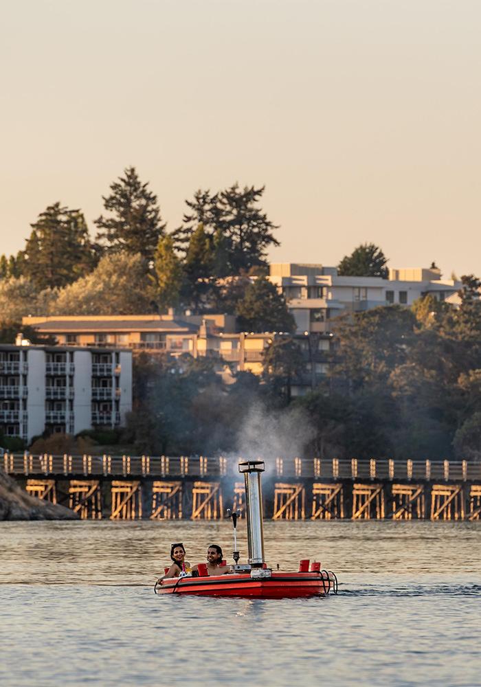 A young couple sails a hot tub boat along the Upper Harbour at sunset in Victoria, BC