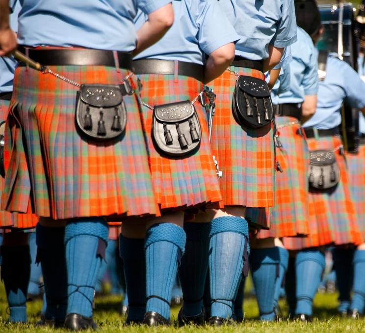 Bagpipe players wearing red kilts and blue shirts and socks marching during the Victoria Highland Games in Victoria, BC