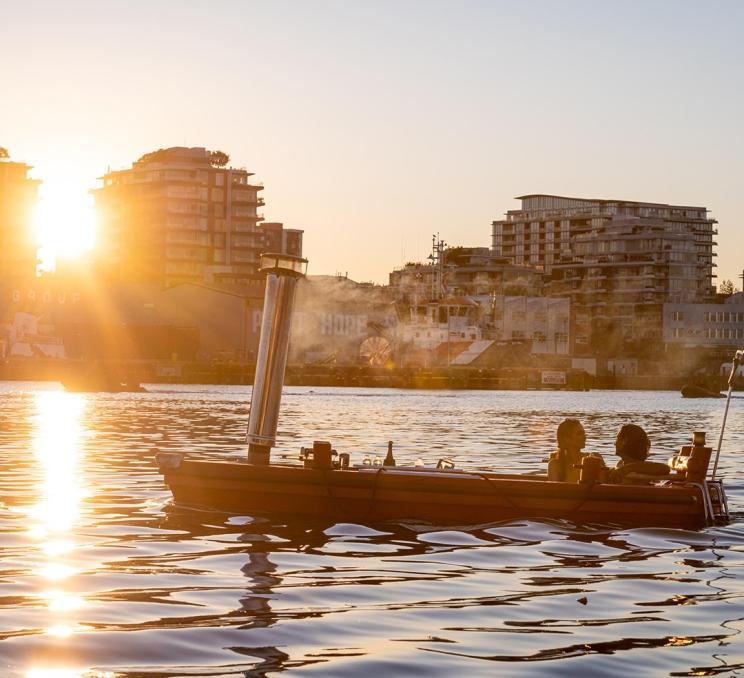 A young couple sails a red hot tub boat through the Upper Harbour during sunset in Victoria, BC