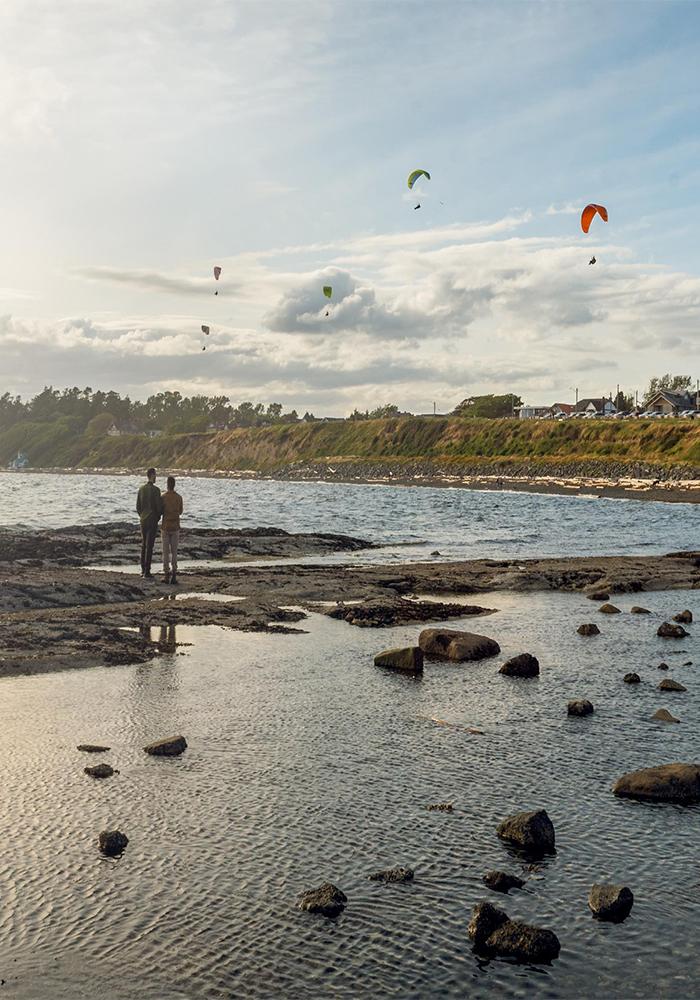 A couple watches the paragliders flying above Dallas Road in Victoria, BC