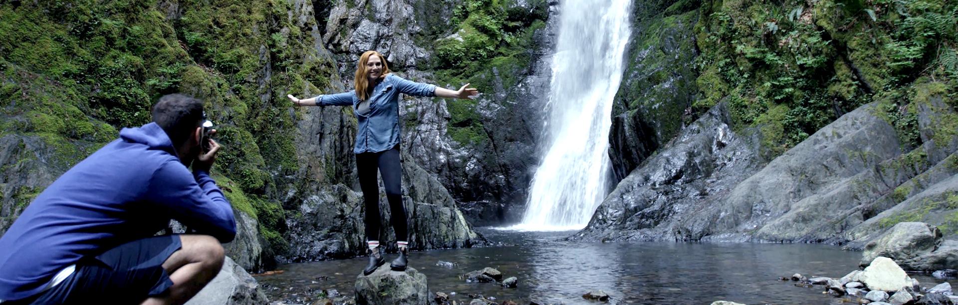 A woman in blue poses for a photo next to Niagara Falls at Goldstream Park in Victoria, BC