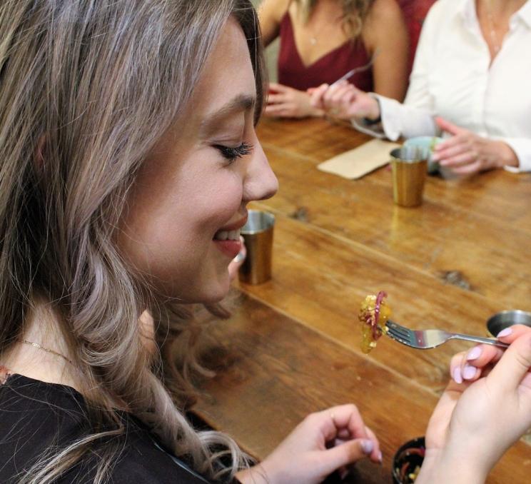 A woman prepares to eat a bite of food during a food tour with Off the Eaten Track in Victoria, BC