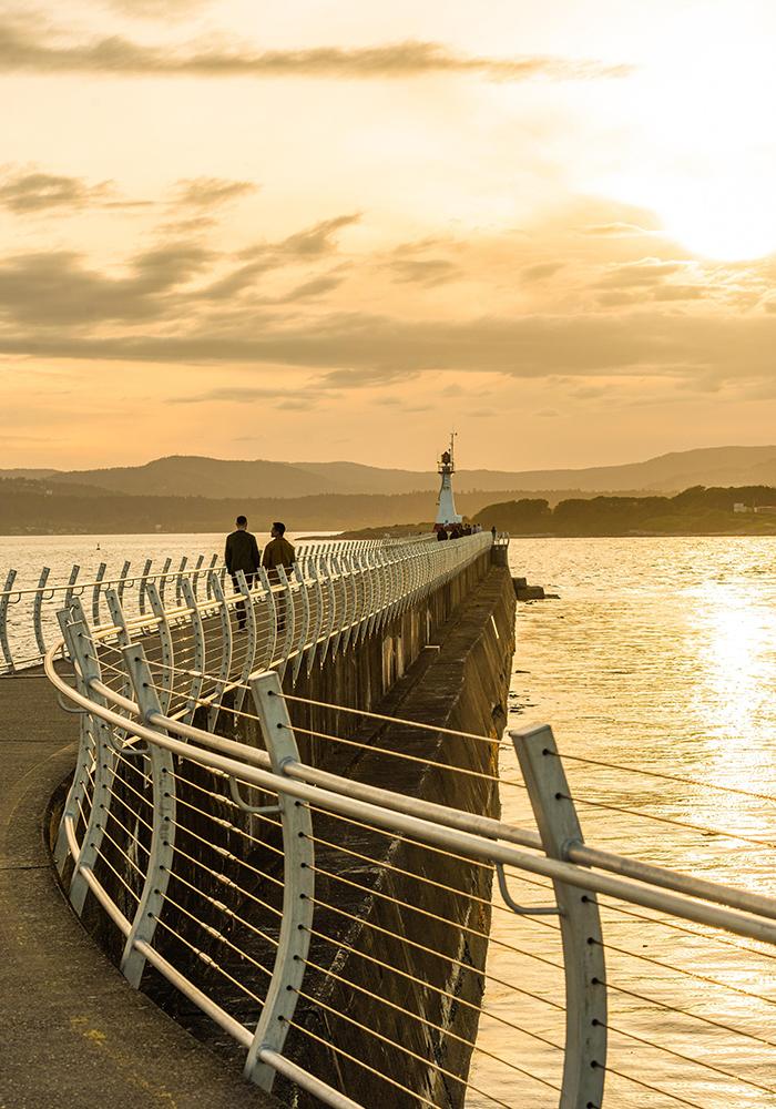 A couple walks along the Ogden Point Breakwater at sunset in Victoria, BC