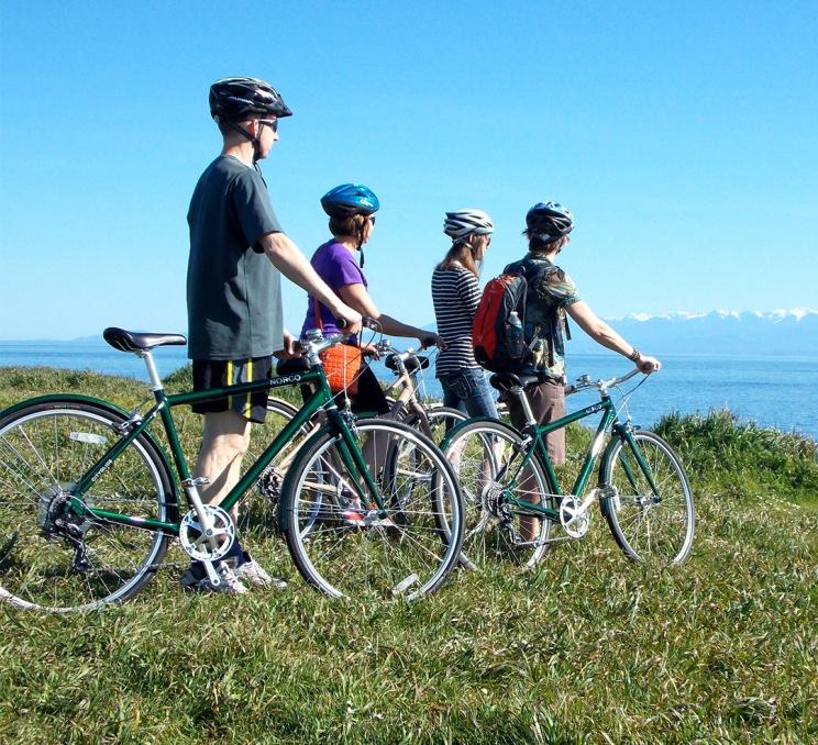 A family with bicycles stands on the grass while looking out over the Salish Sea