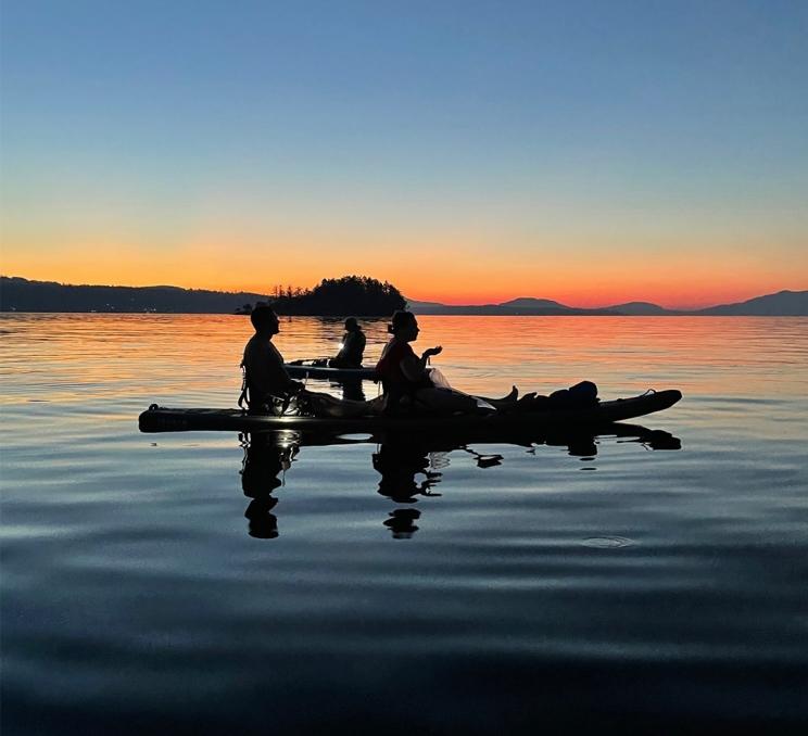 A couple sits atop their paddleboards and watches the sunset in Victoria, BC