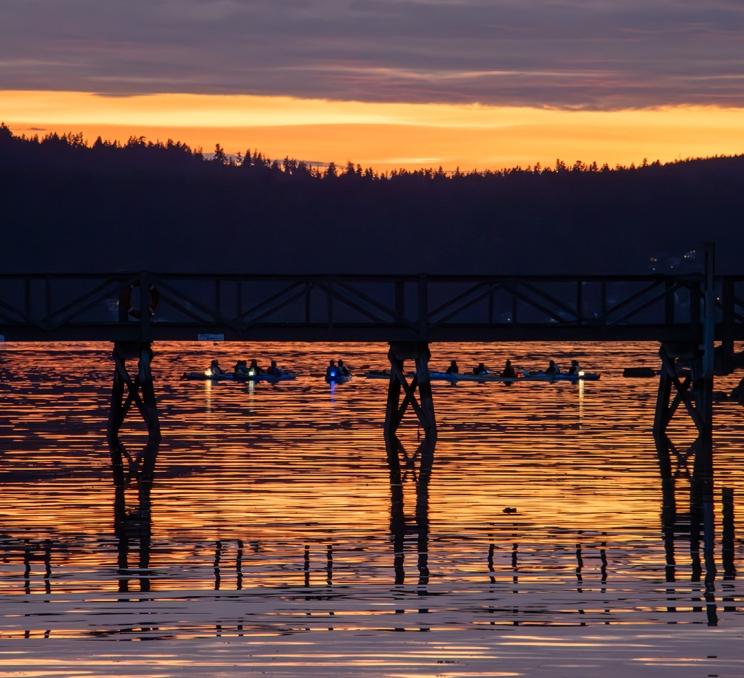 A sunset kayaking tour with Pacifica Paddle Sports gathers on the waters of the Salish Sea off the coast of Victoria, BC