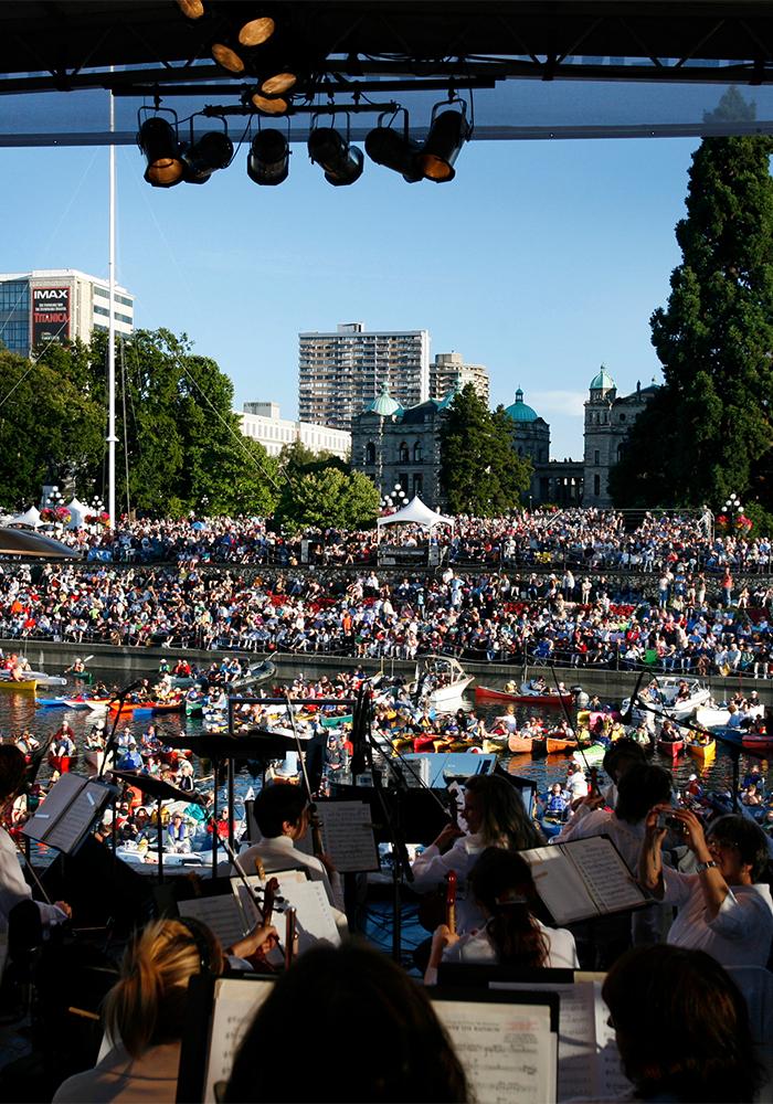 An orchestra performs aboard a barge in Victoria's Inner Harbour as onlookers from the shoreline watch the performance
