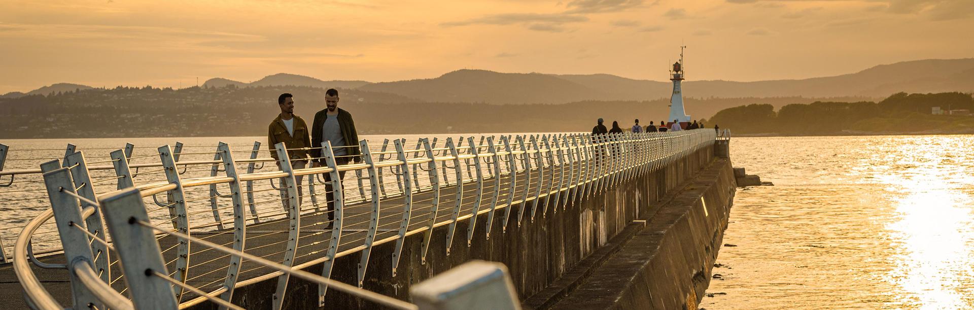 A LGBTQ+ couple walks hand-in-hand along the Ogden Point Breakwater in Victoria, BC