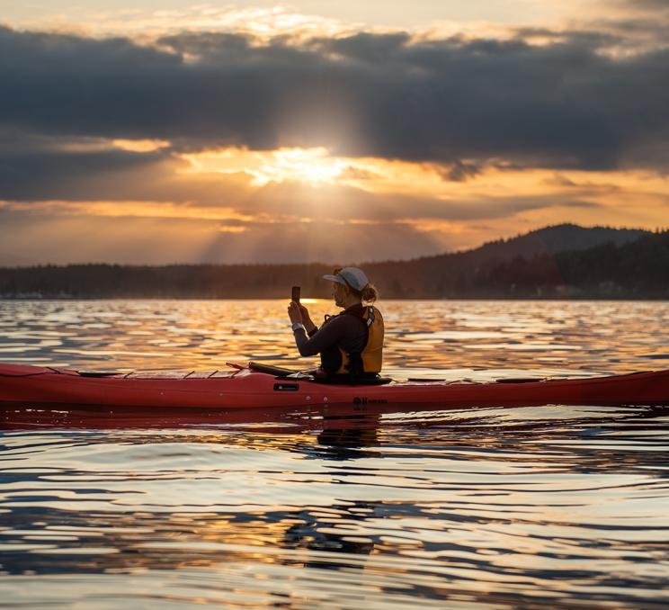 A kayaker in a red kayak takes a photo during a sunset paddle in Victoria, BC