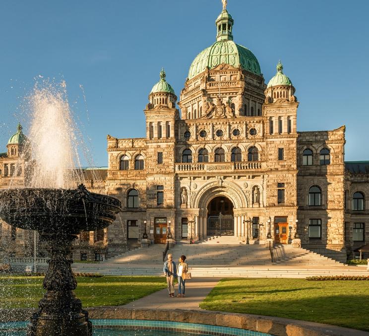 A couple walks toward the Centennial Fountain at the BC Parliament Buildings in Victoria, BC