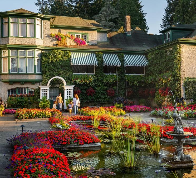 A family walks through a garden at The Butchart Gardens with the Heritage Building in the background in Victoria, BC