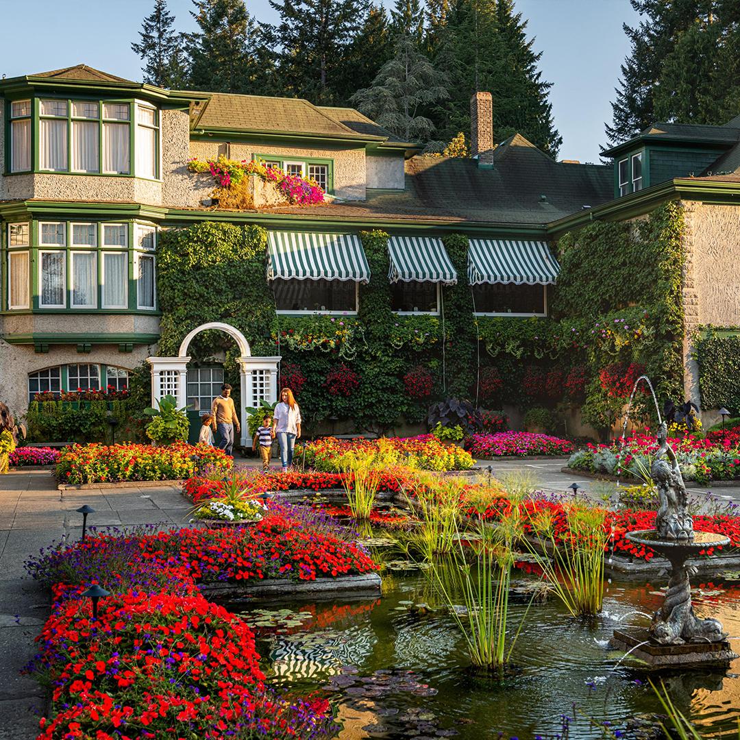 A family walks through a garden at The Butchart Gardens with the Heritage Building in the background in Victoria, BC