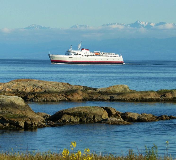 The MV Coho of Black Ball Ferry Lines sails across the Salish Sea with the Olympic Mountain range in the background in Victoria, BC