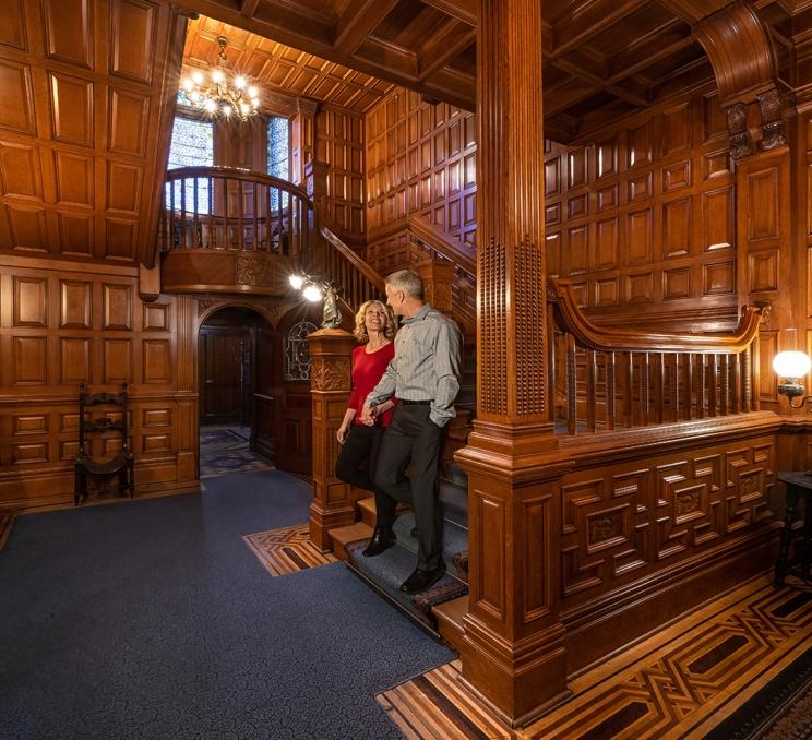 A couple walks hand-in-hand down the stairs at Craigdarroch Castle in Victoria, BC