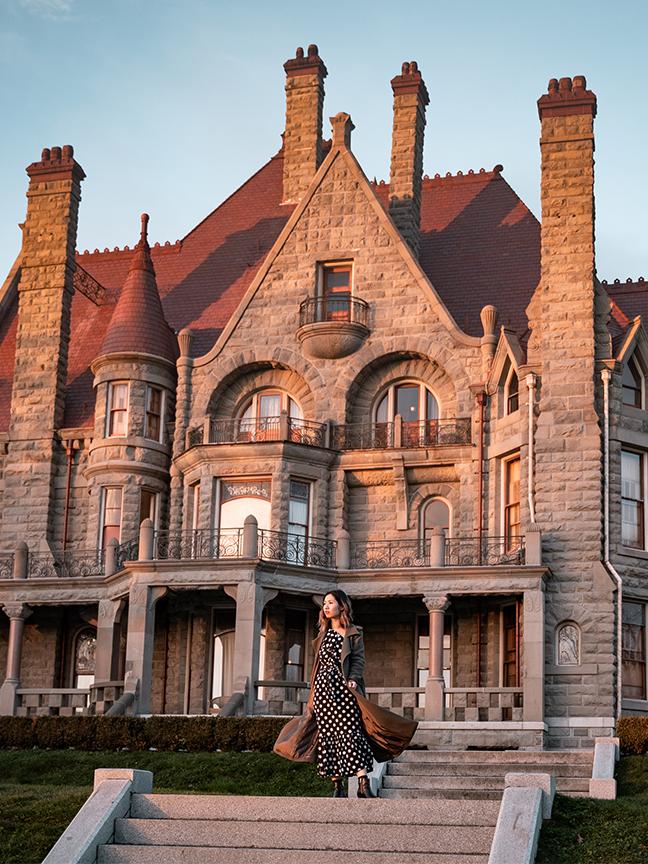 A woman stands outside Craigdarroch Castle at sunset in Victoria, BC