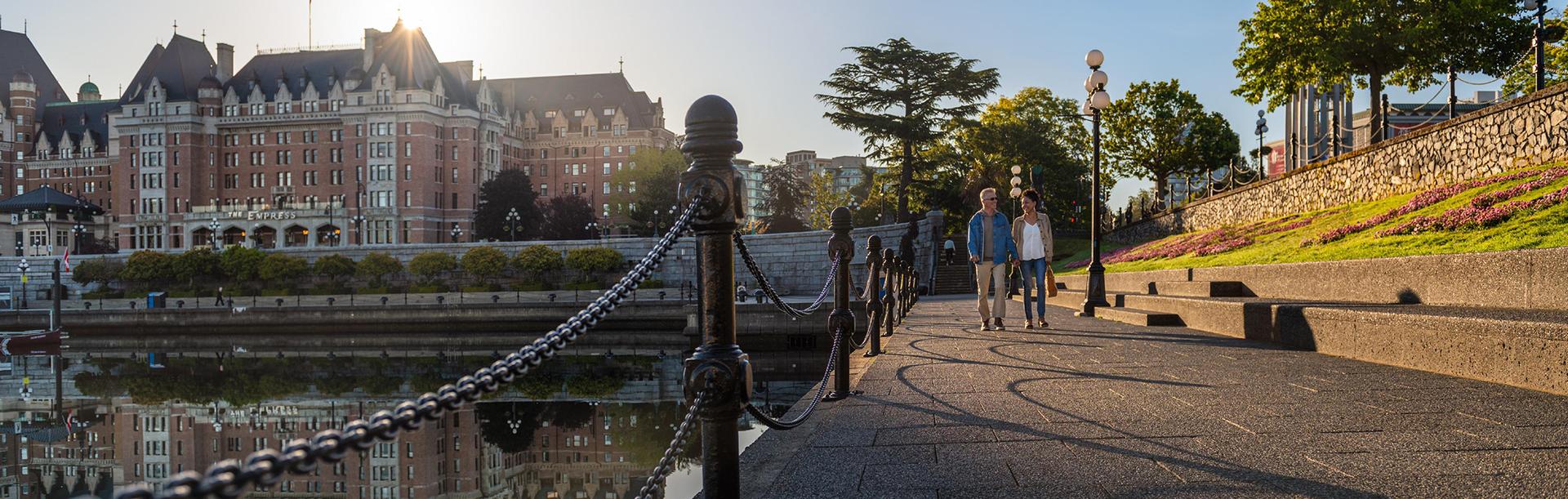 A couple walks along the lower causeway of the Inner Harbour with the Fairmont Empress in background in Victoria, BC