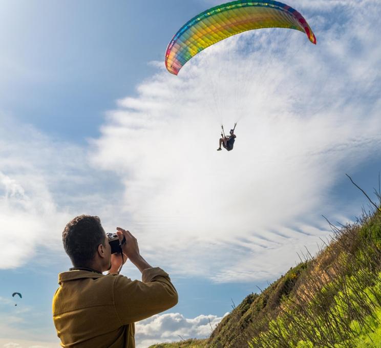 A man takes a photo of a paraglider along Dallas Road in Victoria, BC
