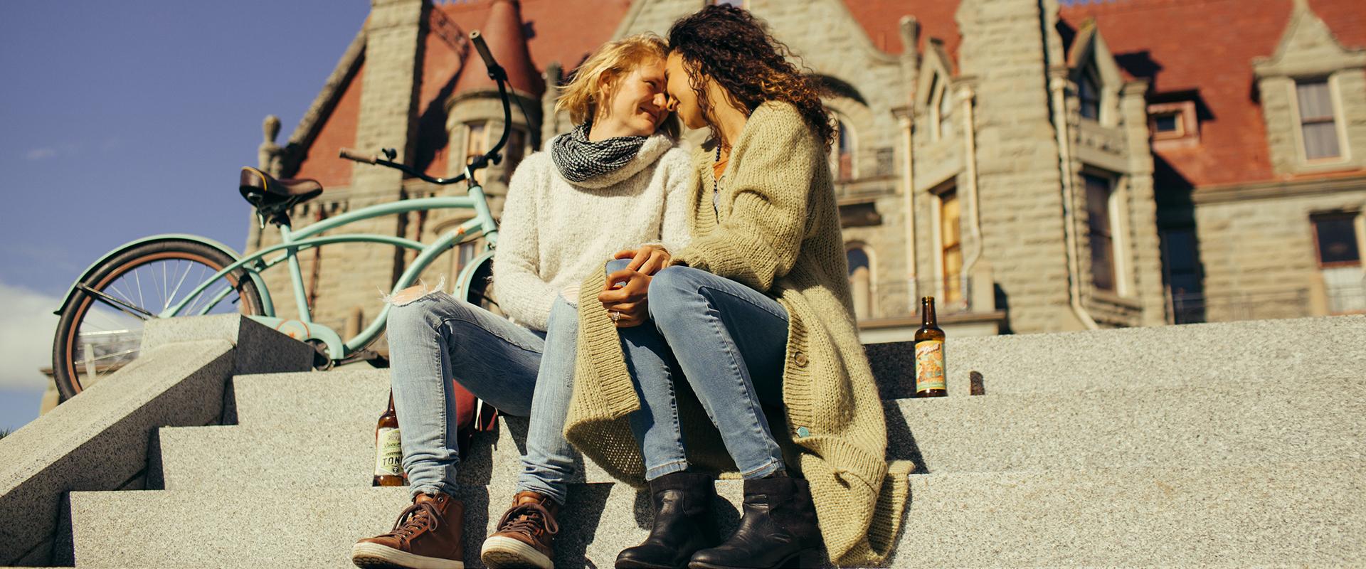 A female couple embraces on the steps outside of Craigdarroch Castle in Victoria, BC