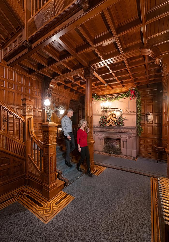 A couple walking down the grand staircase in Craigdarroch Castle Historic House Museum in Victoria, BC during the holiday season