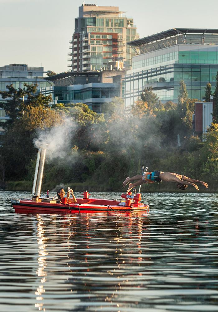 A man dives off a hot tub boat into the upper harbour while his partner takes a photo in Victoria, BC