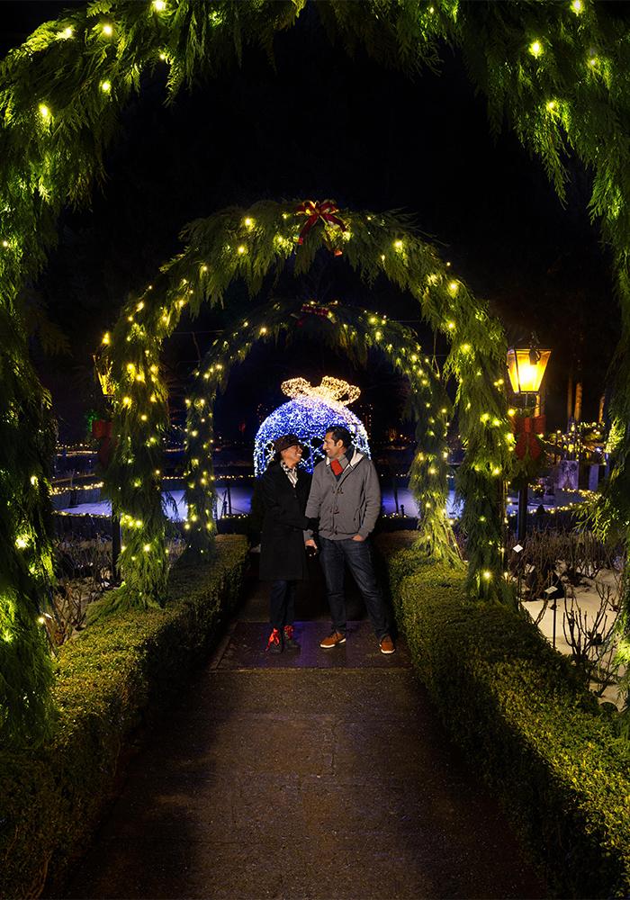 A couple walks hand-in-hand beneath illuminated arches at The Butchart Gardens in Victoria, BC