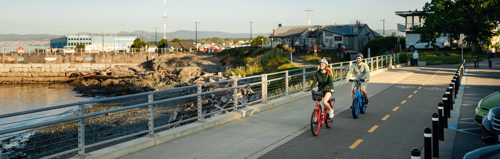 A couple riding ebikes near the Ogden Point Breakwater along the bike path on Dallas Road at sunrise in Victoria, BC