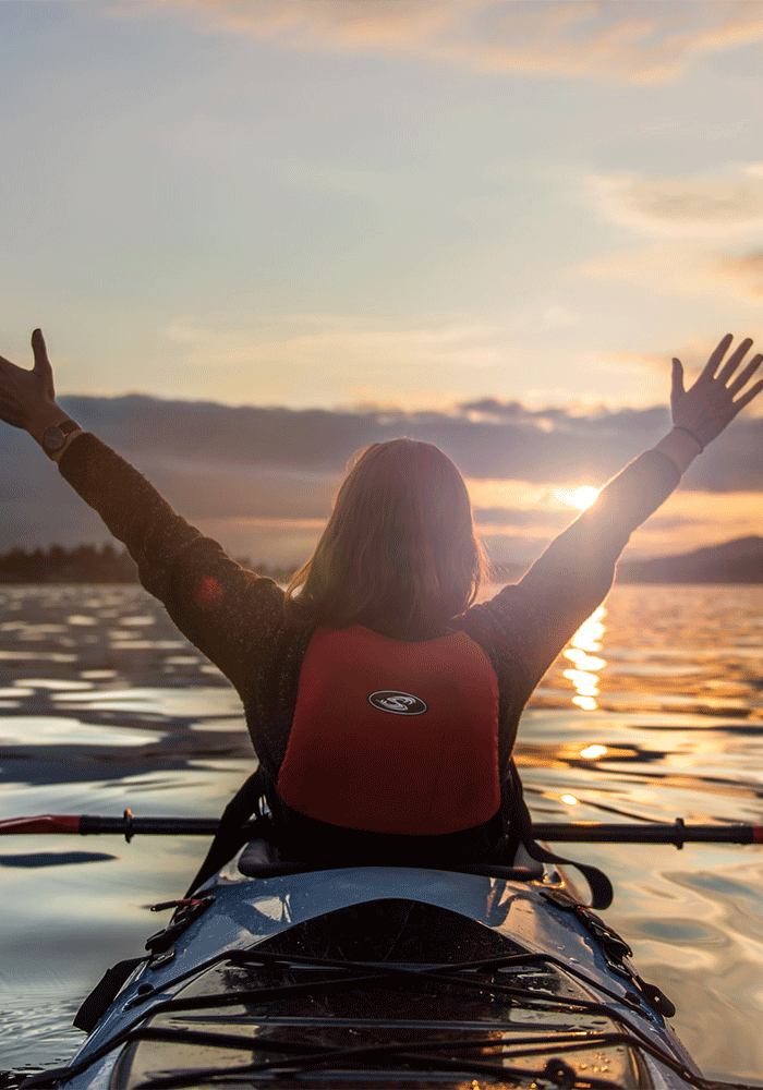 A kayaker waves their hands in the air while paddling at sunrise on the Salish Sea in Victoria, BC