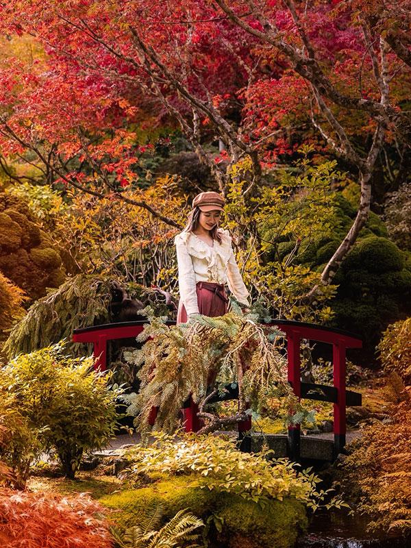 A woman stands on a bridge in the Japanese Garden while admiring the fall foliage at The Butchart Gardens in Victoria, BC