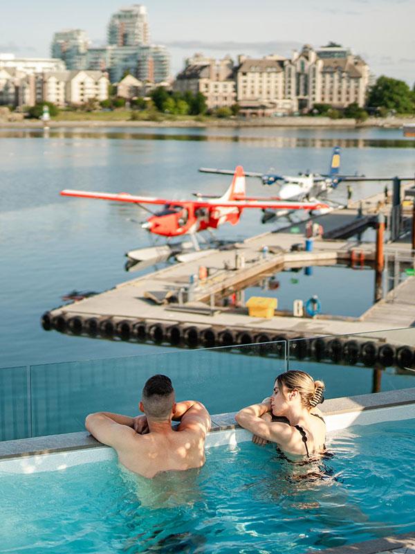 A couple soaks in a hot tub overlooking the Inner Harbour and red seaplane while at HAVN Saunas in Victoria, BC