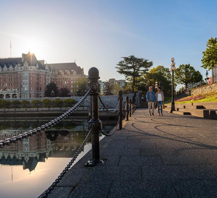 A couple walks hand-in-hand along the Lower Causeway of the Inner Harbour at sunrise in Victoria, BC