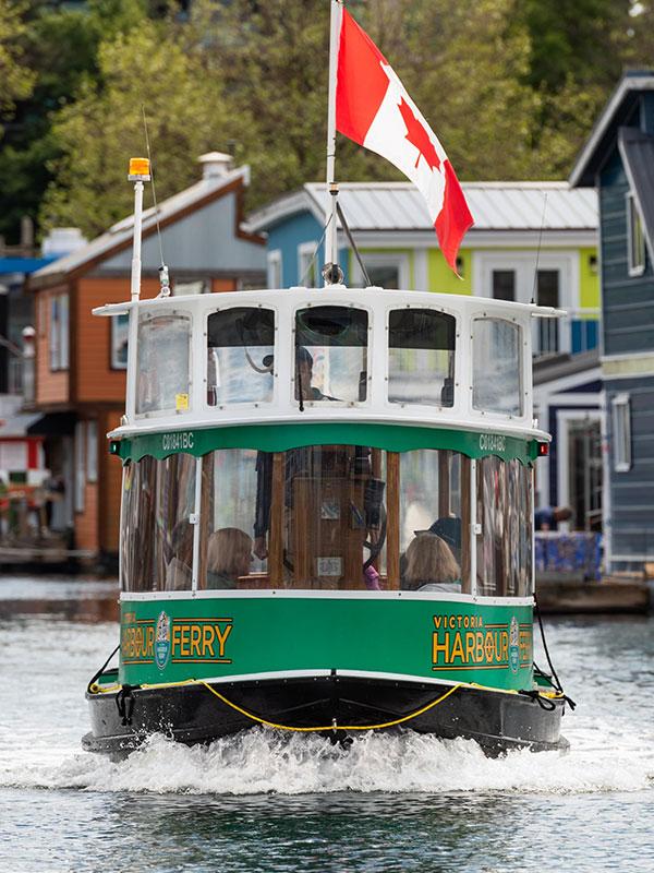 A green Victoria Harbour Ferry departing from the dock at Fisherman's Wharf, a colourful float home community, in Victoria, BC