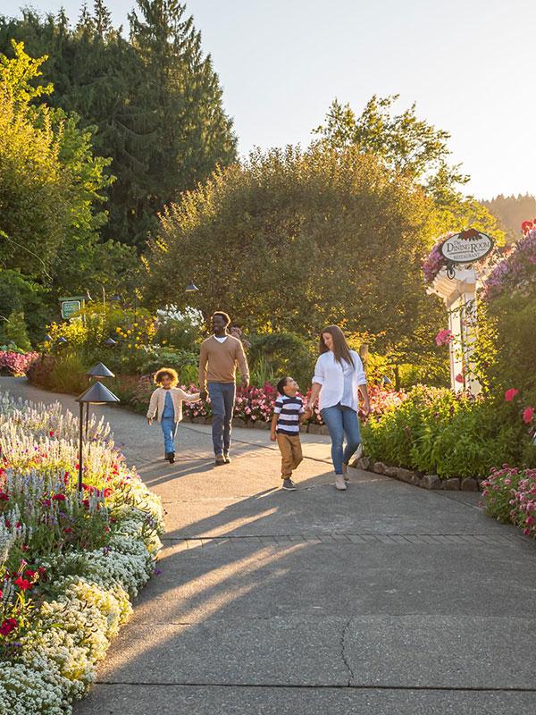 A young family walks hand-in-hand through along a pathway at The Butchart Gardens in Victoria, BC